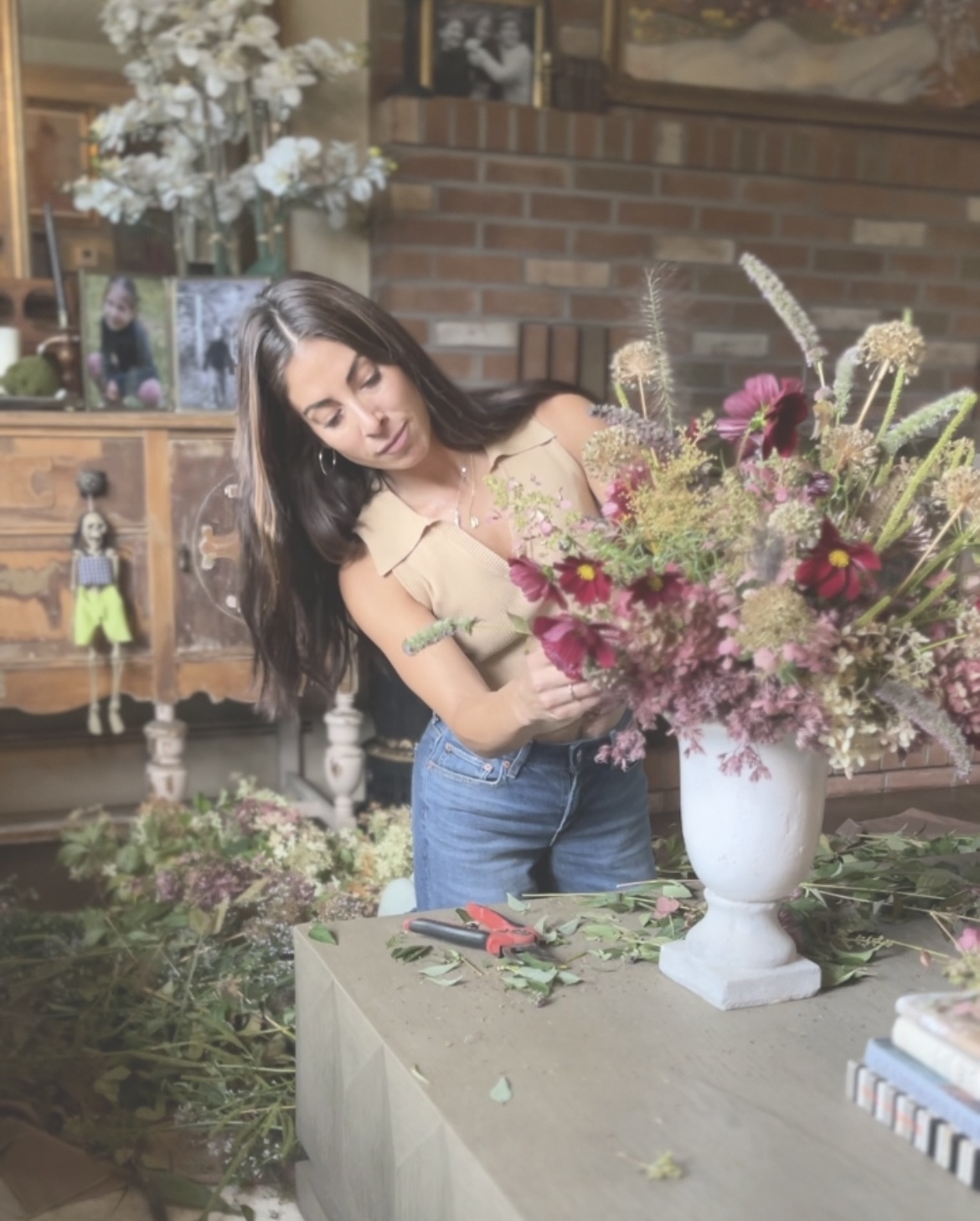 Tori arranging garden-grown flowers in a white urn against a brick wall